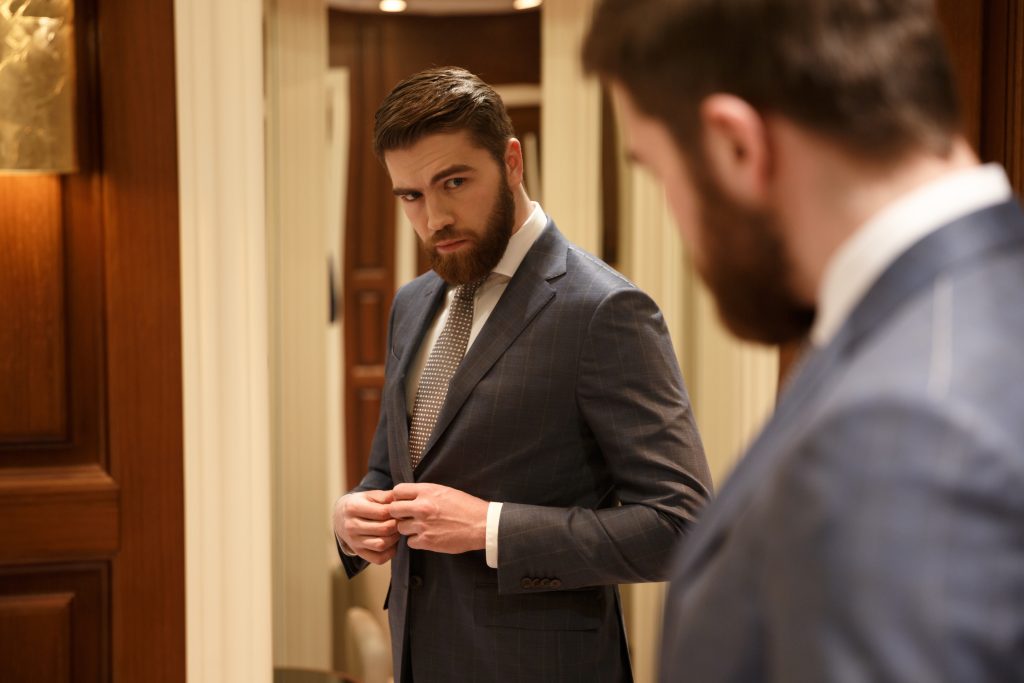 Lelaki bersut profesional melihat cermin, mencerminkan kepimpinan melalui teladan dan pemakaian seperti pemimpin korporat.