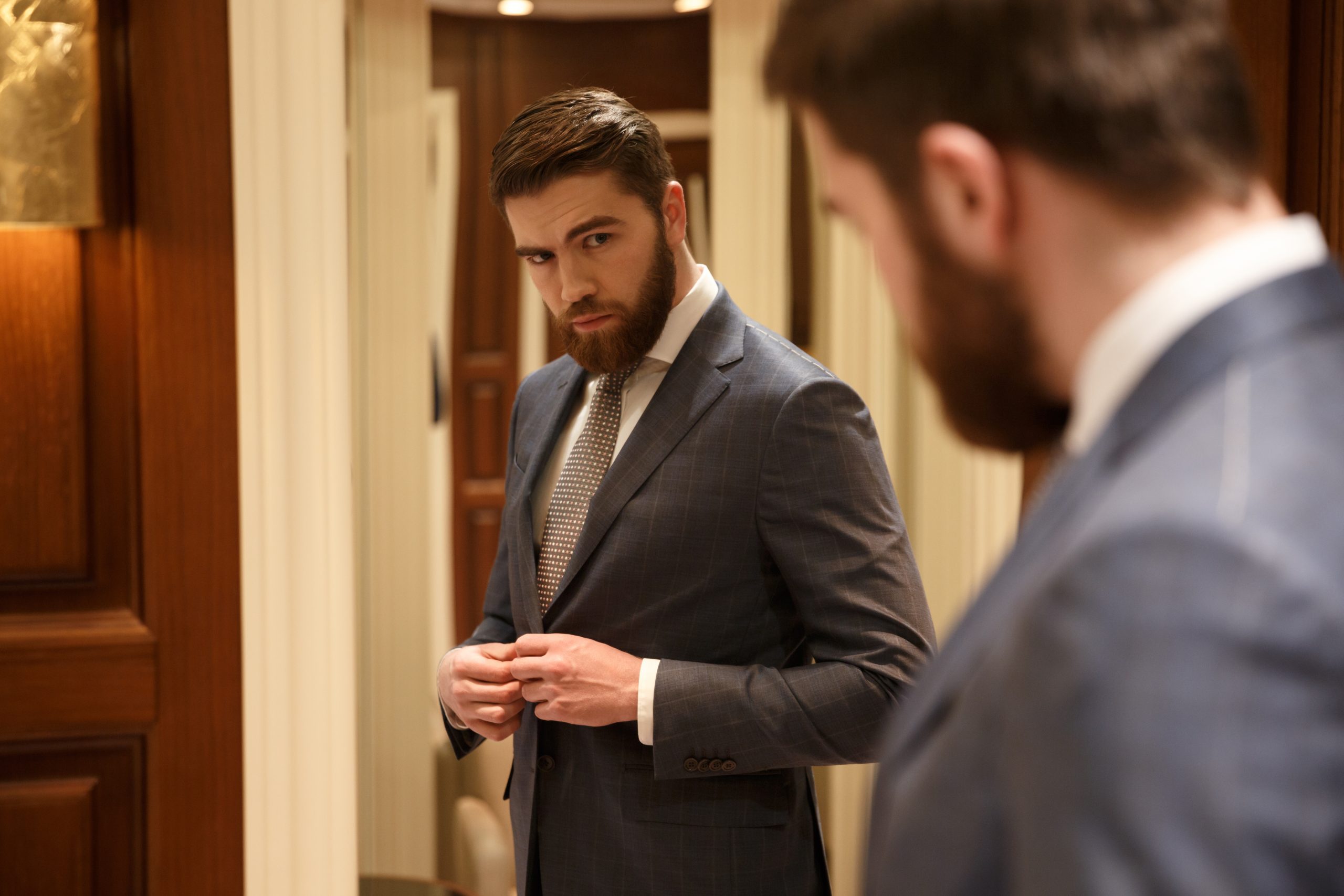 Lelaki bersut profesional melihat cermin, mencerminkan kepimpinan melalui teladan dan pemakaian seperti pemimpin korporat.